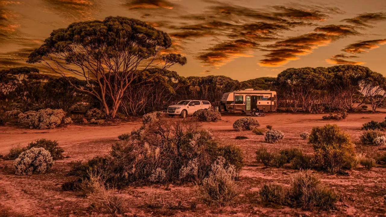 4WD and caravan parked in red-dirt scrub at sunset.